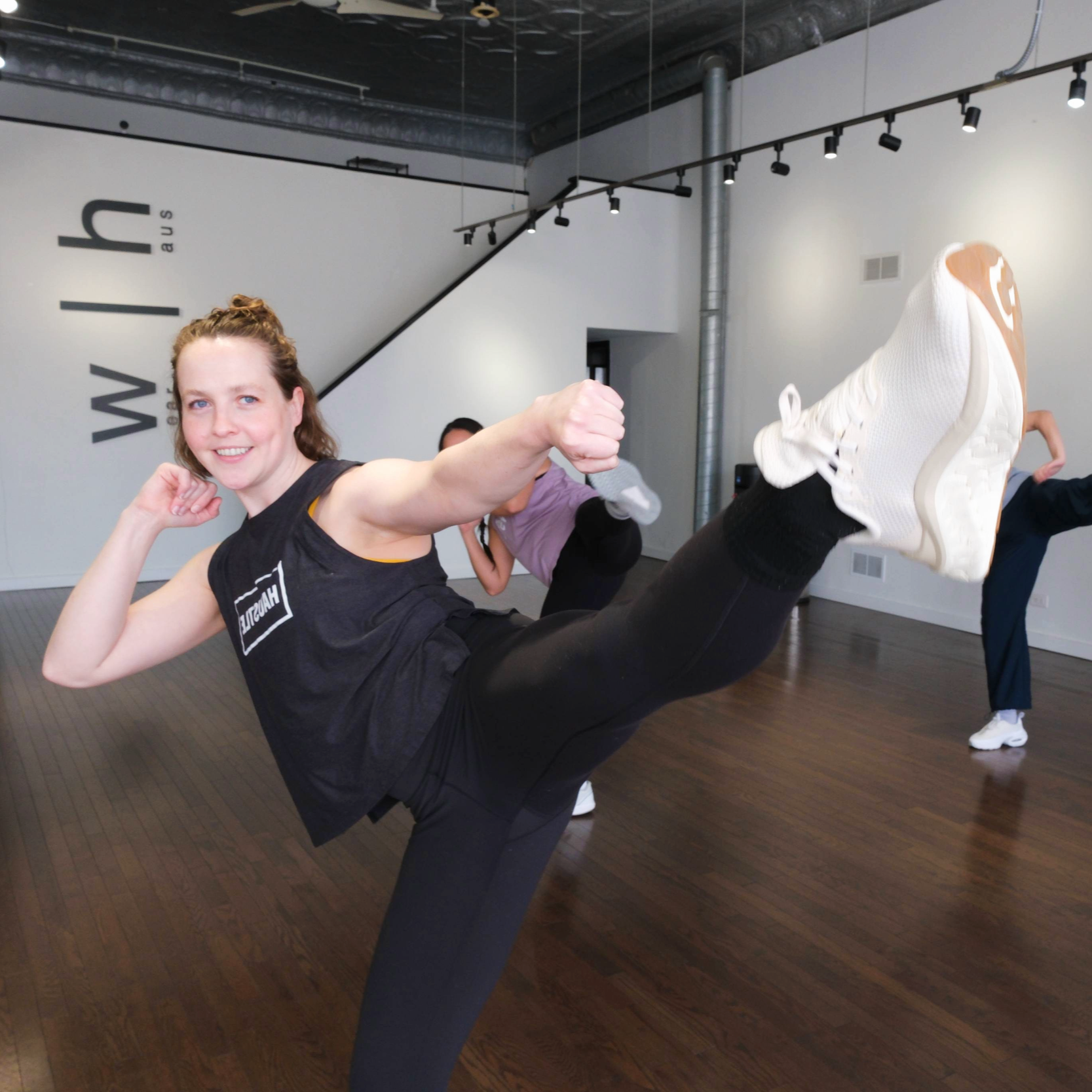 Smiling woman leading group through a kickboxing routine.