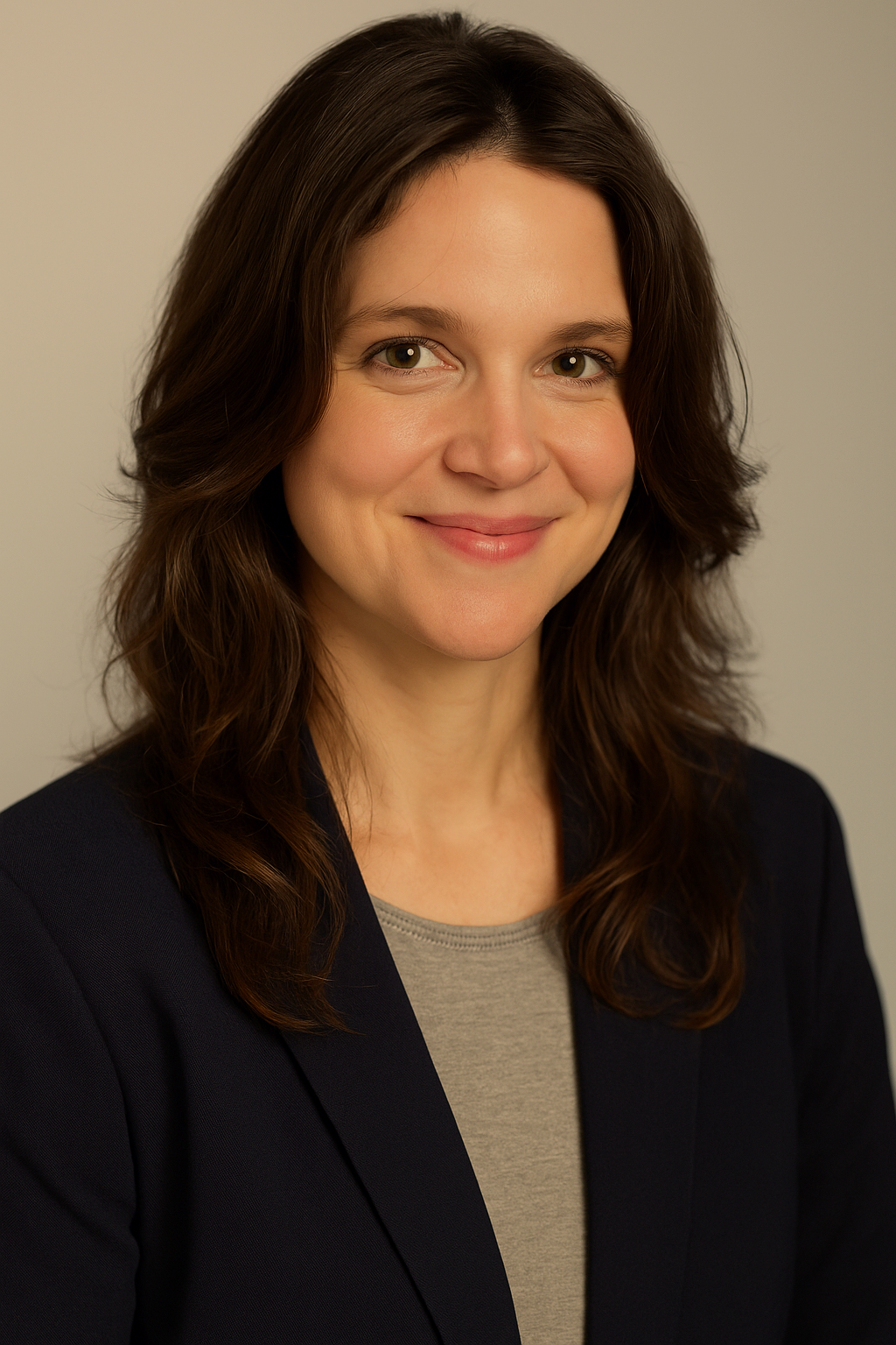 Professional headshot of a smiling woman with shoulder-length brown hair, wearing a dark blazer and a gray top, against a neutral background.