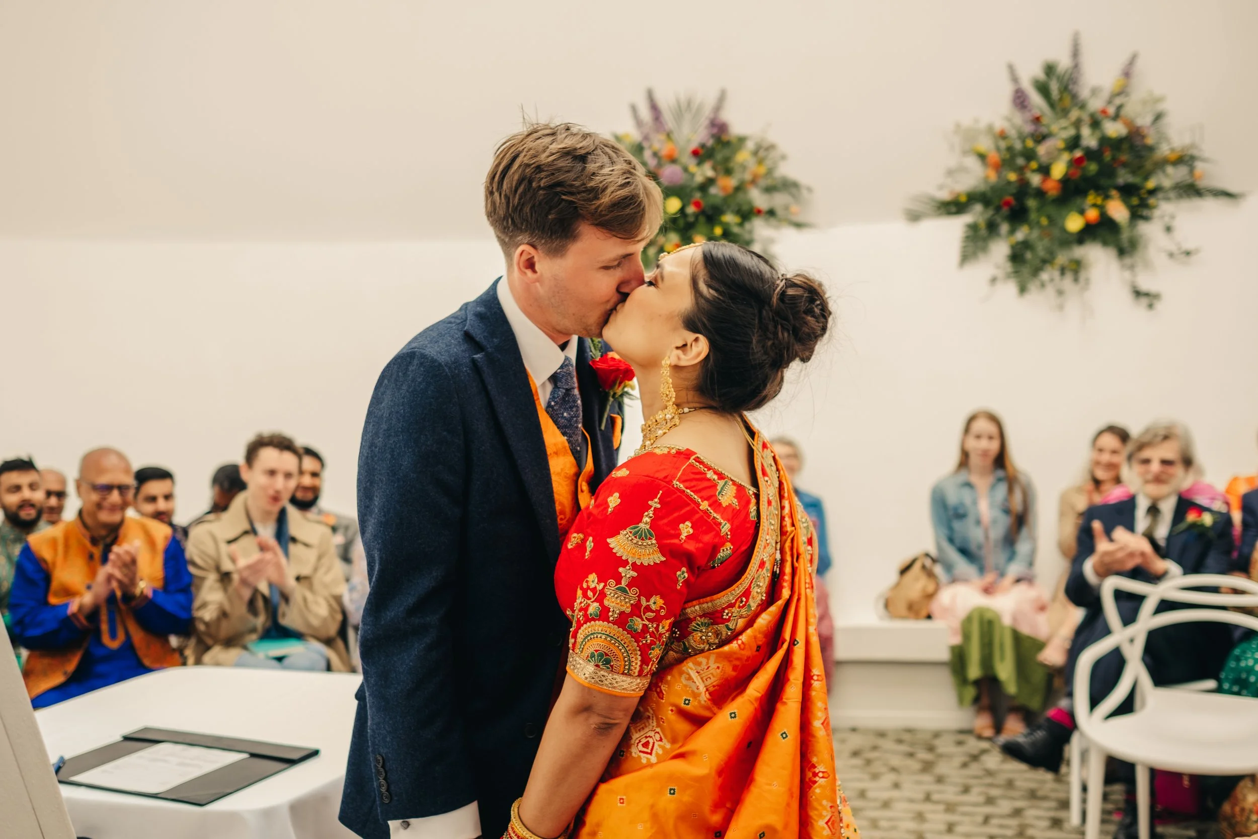 A couple kissing during a wedding ceremony with guests clapping in the background. Tremenheere Sculpture Gardens, Cornwall,  Cornwall Wedding Venue,  Cornwall Wedding Photographer.