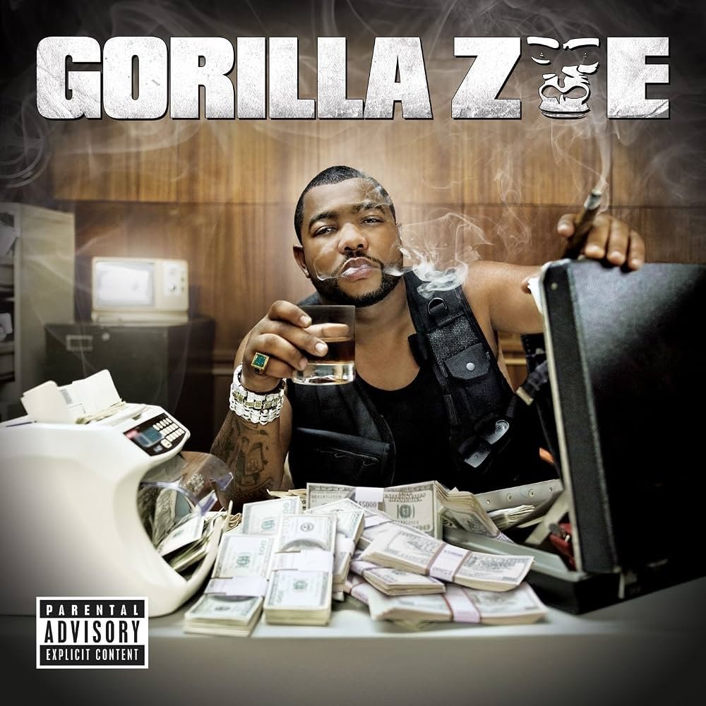 Album cover of the rapper Gorilla Zoe, showing him sitting at a desk with stacks of money, smoking a cigarette, holding a glass of liquor, and looking at a computer monitor. The background features a wooden wall with the artist's name and a gorilla face logo.