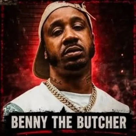 Portrait of Benny the Butcher wearing a backward cap, gold chain, and earrings with a dark red background.