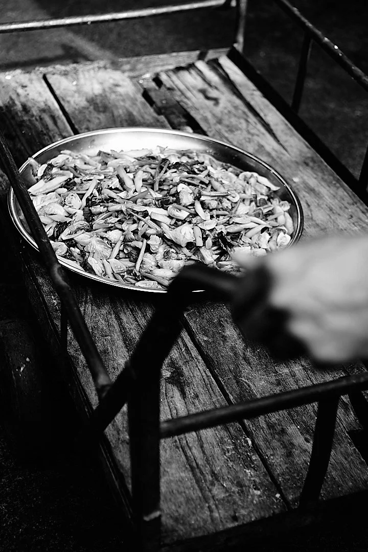 A wide pan of chopped vegetables at a night market stall, a hand reaching in from the edge of the frame. Someone is about to eat. Everything else can wait.