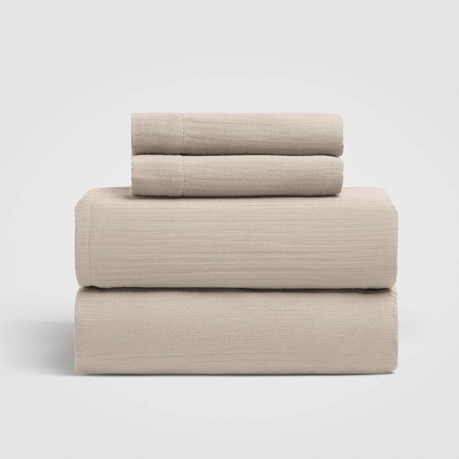 Stacked beige upholstered cushions and pillows on a white background.