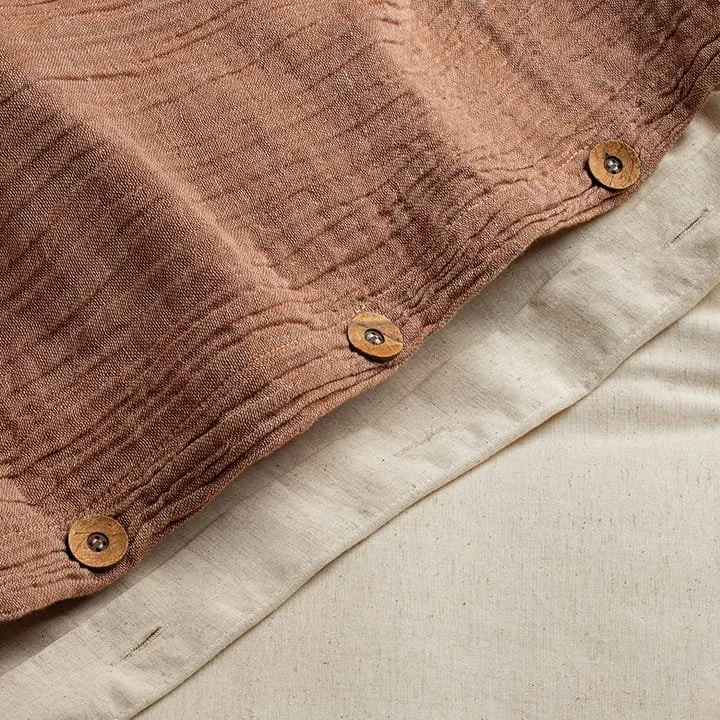 Close-up of a beige fabric with a salmon-colored textured draped cloth secured with three small round wooden buttons with black screws.