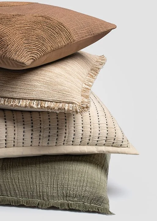 Stack of four decorative throw pillows in neutral tones and textured patterns.