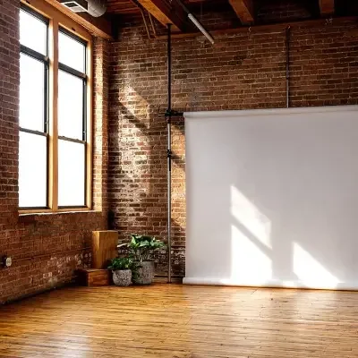 Empty photo studio with brick walls, large industrial windows, hardwood floor, and a roll-up backdrop.