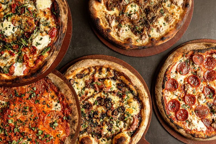 Five different pizzas on wooden boards with various toppings, including pepperoni, herbs, and assorted cheeses.