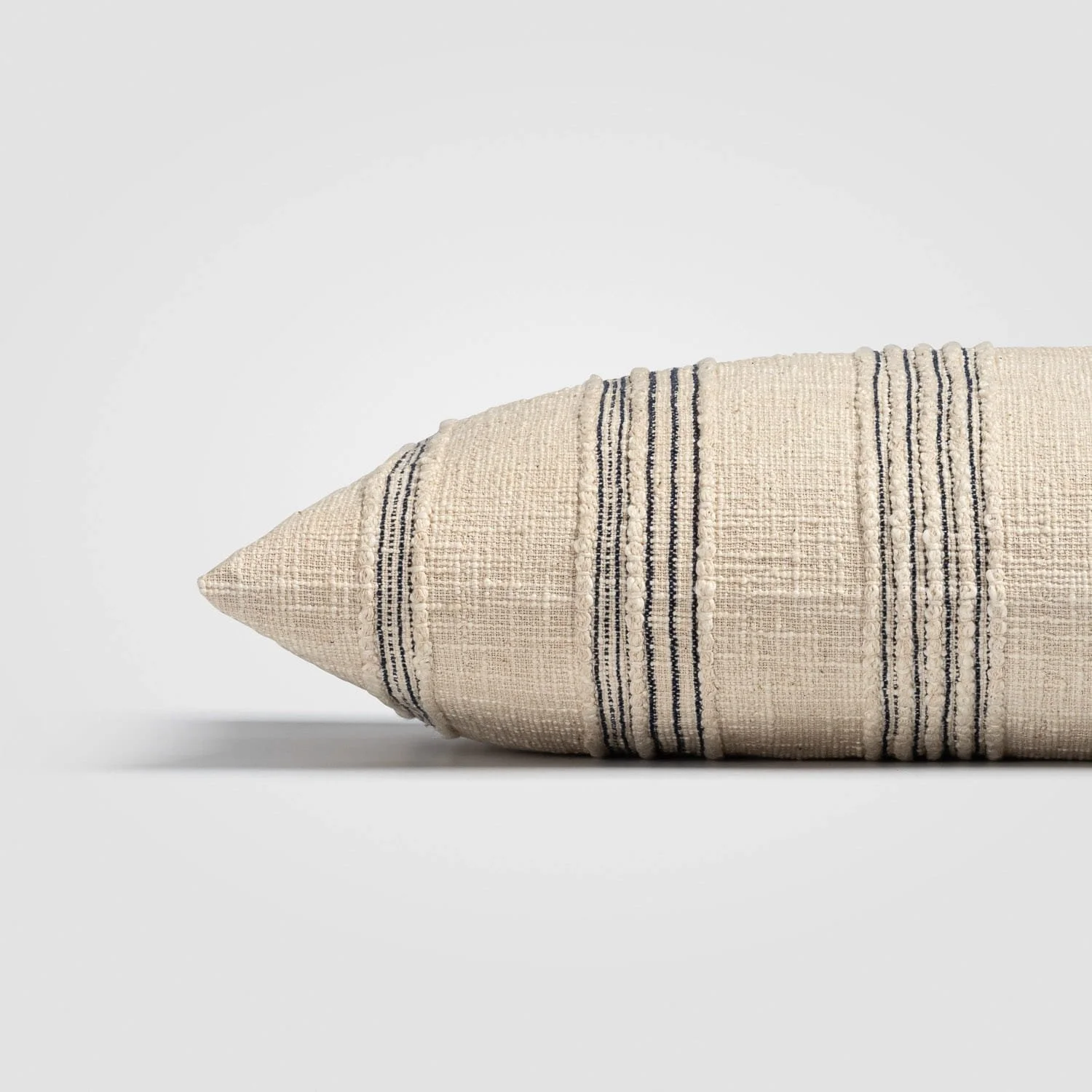 Close-up of a beige decorative pillow with black and beige striped pattern on a plain white background.