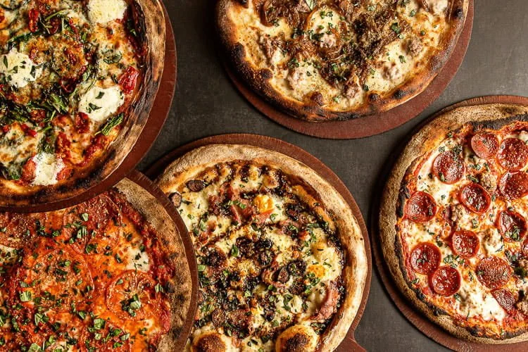 Four different pizzas on wooden boards, featuring various toppings such as pepperoni, sausage, vegetables, and cheese.