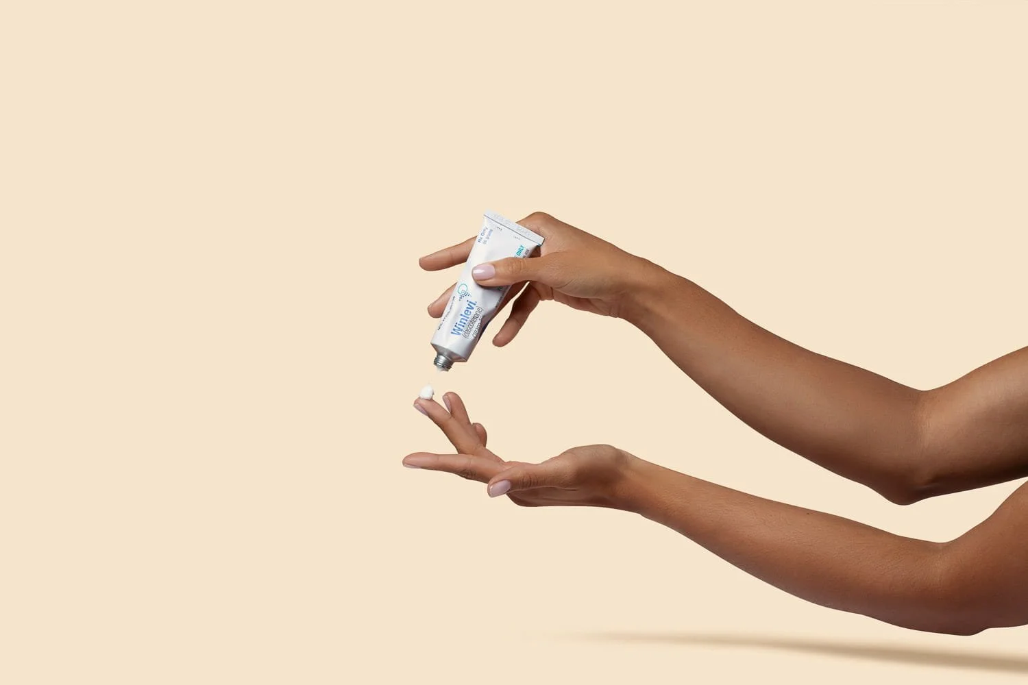 Person squeezing hand cream onto their finger with a beige background.