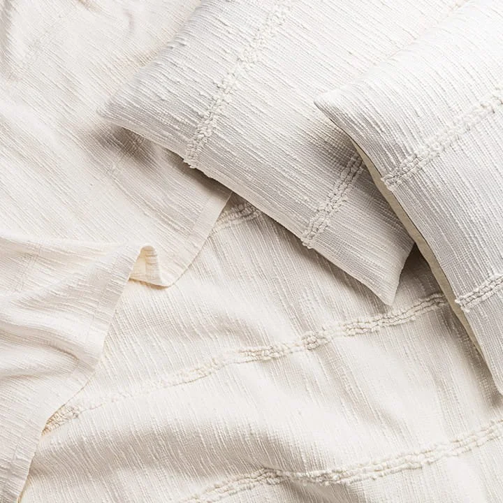 Close-up of cream-colored, textured bed sheets and pillowcases with embroidered details.