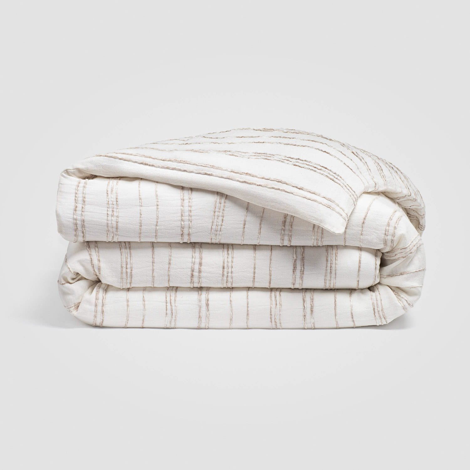 Stacked white and beige striped bedsheets neatly folded on a plain white background.