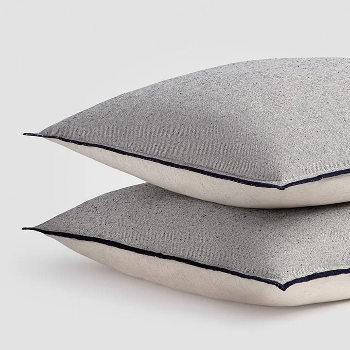 Two stacked decorative pillows with gray and white fabric, black piping along the edges, on a plain white background.