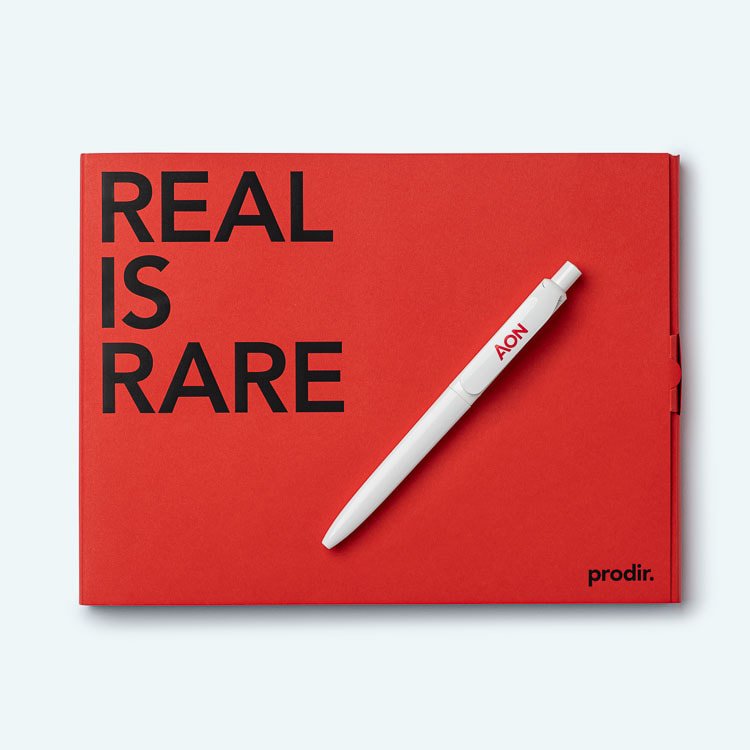 A red notebook with black text that says "REAL IS RARE" and a white pen with red text that says "AON" placed on it.