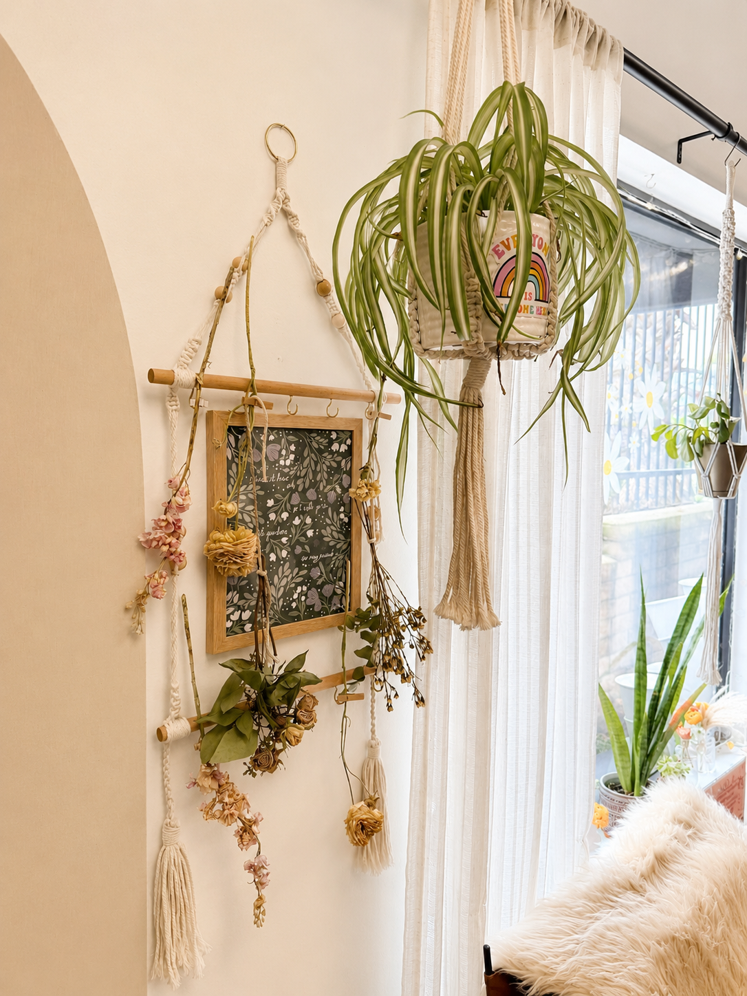 Decorative wall with hanging flower garlands, a framed blackboard, and potted plants near a window with sheer curtains