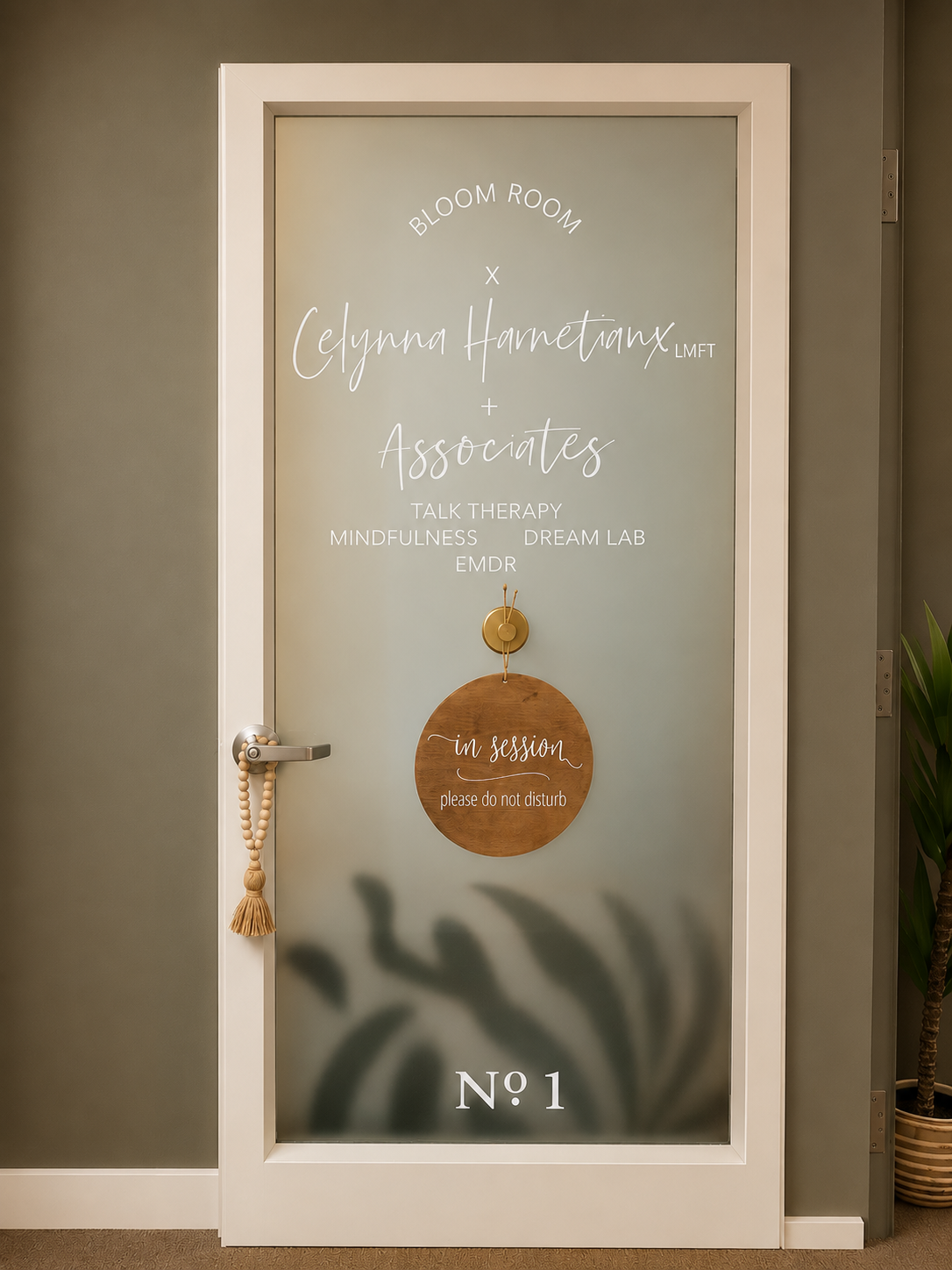 Decorative door with frosted glass, white frame, text about a therapy practice, a wooden 'in session' sign hanging on the door, and a potted plant to the right.