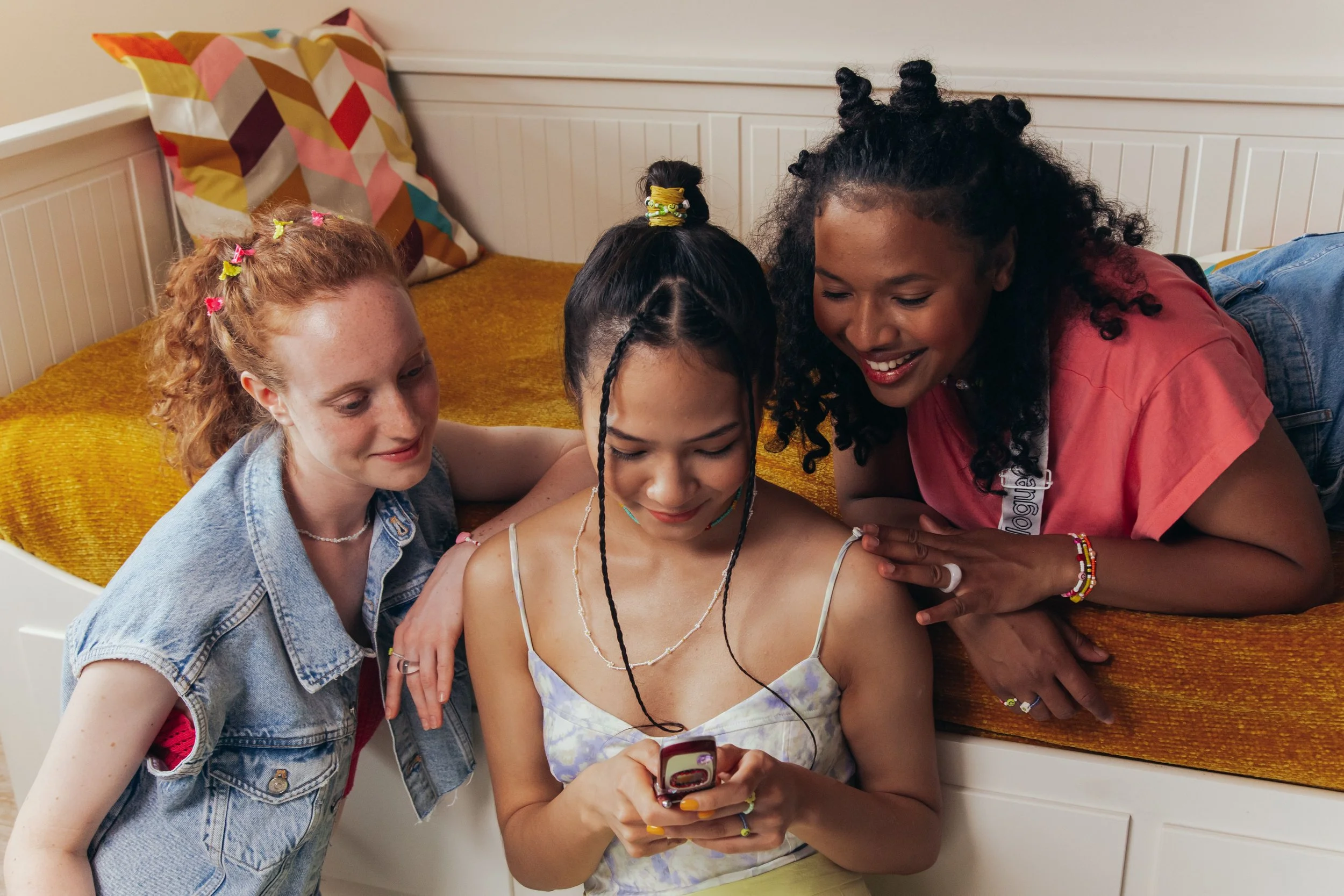 three young femme presenting people look at the content on a phone