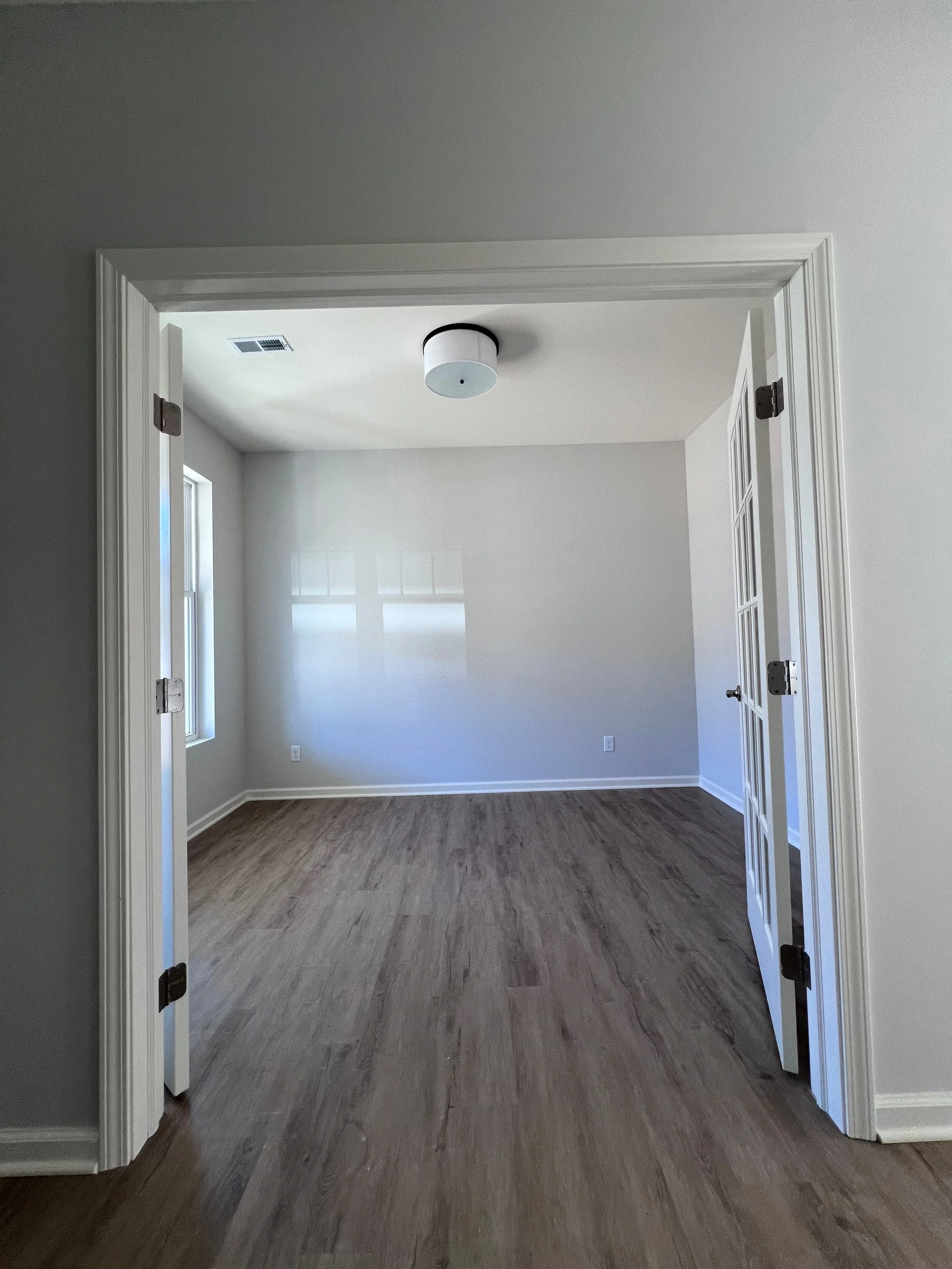 Empty room with hardwood floors, gray walls, white trim, a ceiling light fixture, and two windows.