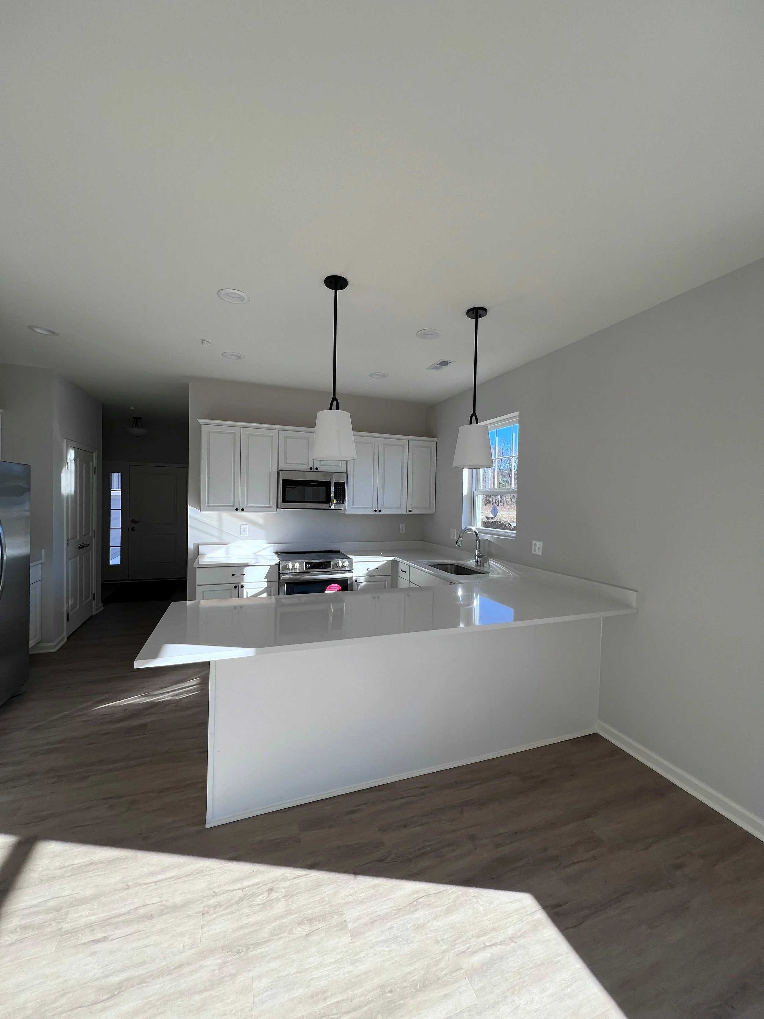 Modern kitchen with white cabinets, stainless steel appliances, pendant lights, and hardwood floors.