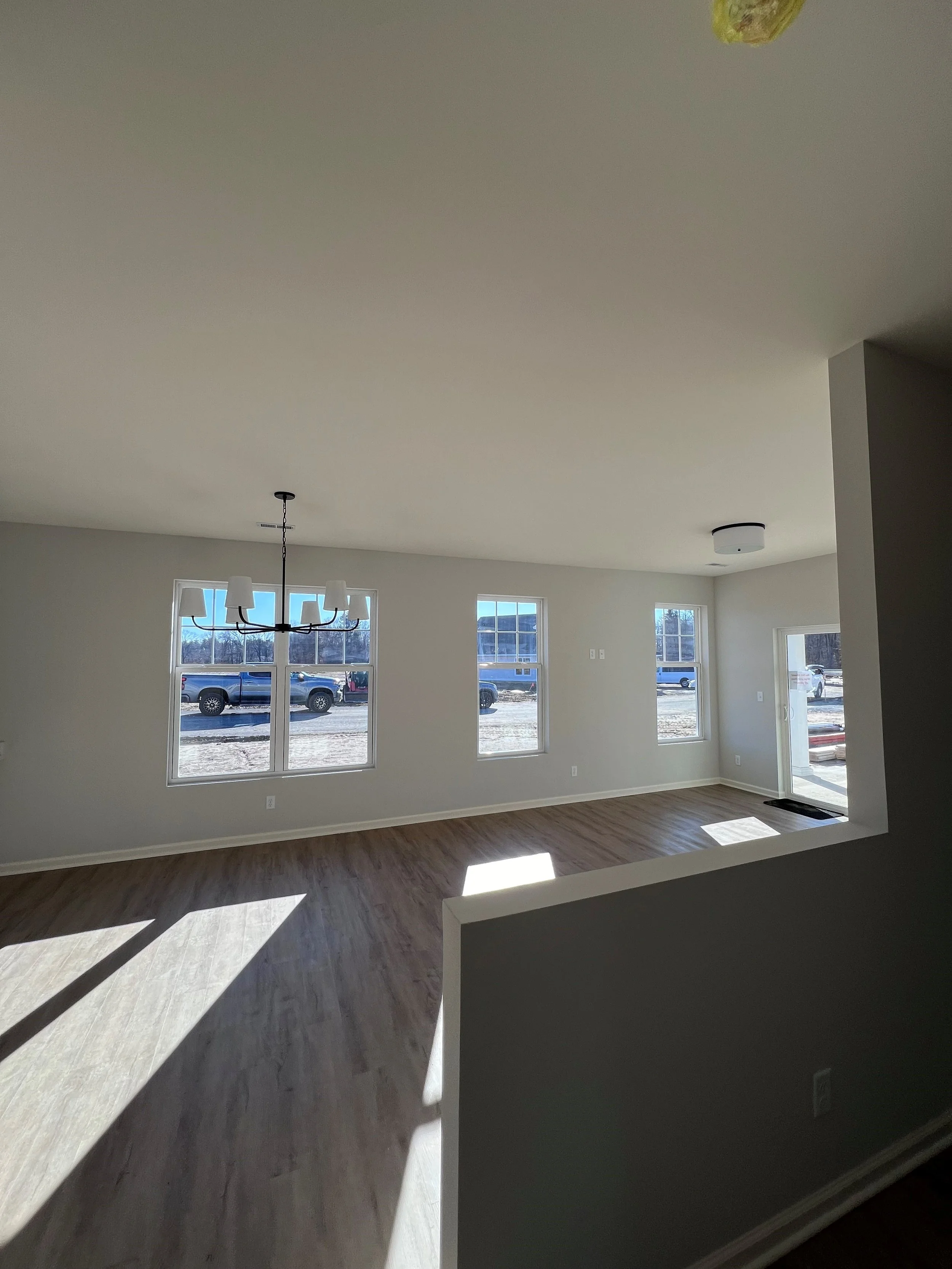 Interior of a new, empty living room with large windows, hardwood floors, and a modern chandelier hanging from the ceiling.