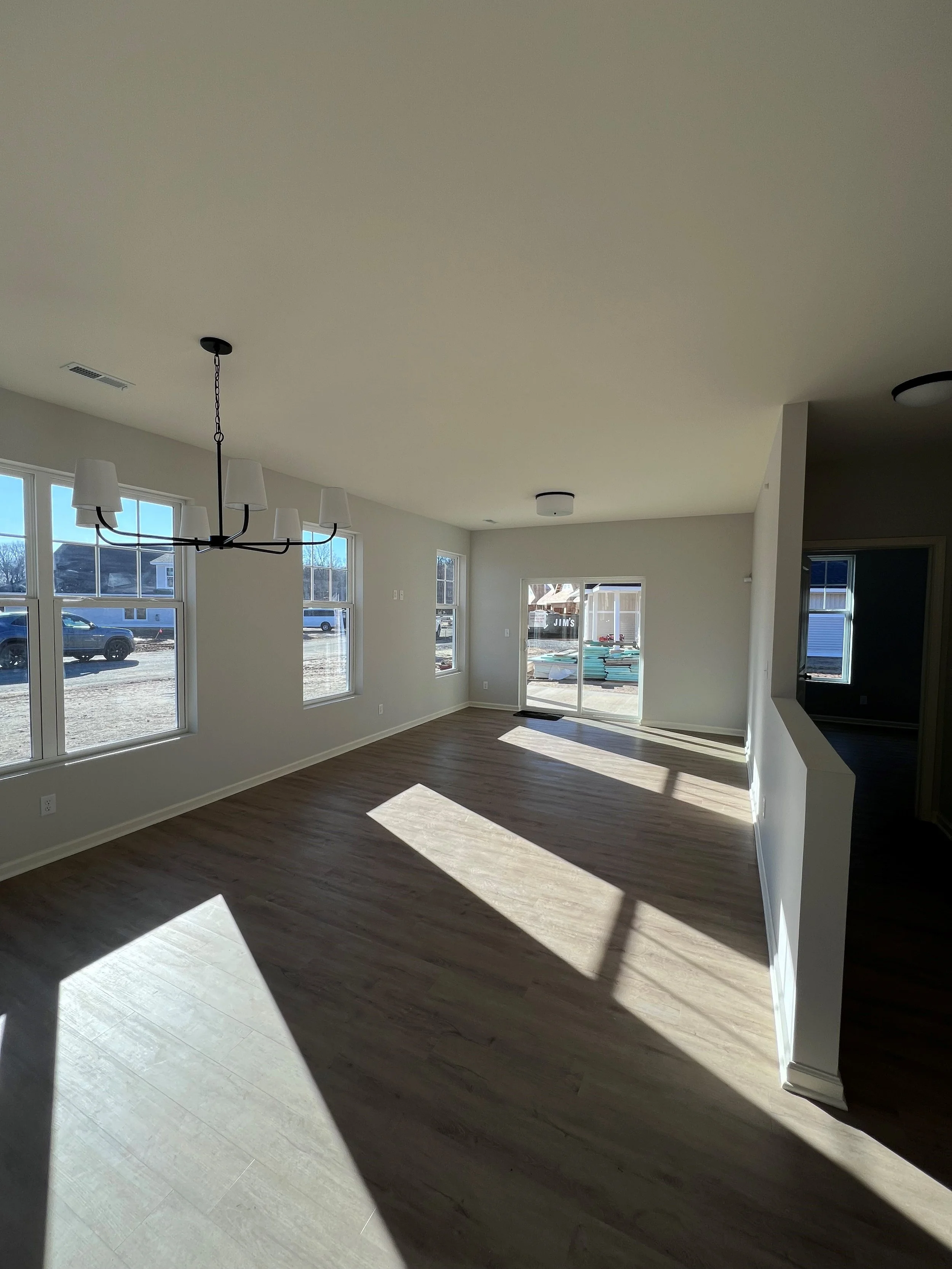 Empty living room with large windows, hardwood floors, and a pendant light fixture.