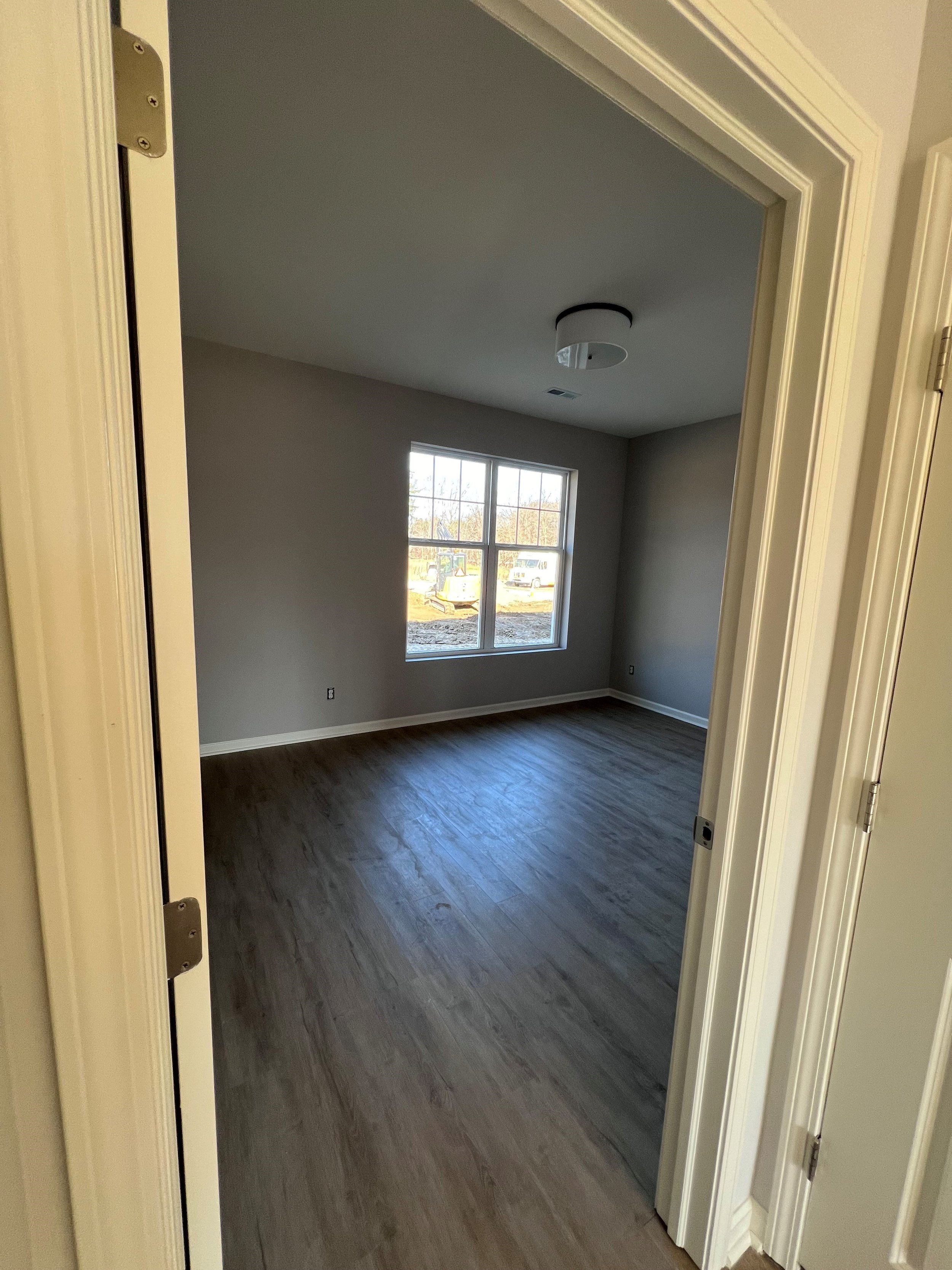 Empty room with a window, gray walls, wood flooring, and a ceiling light fixture.