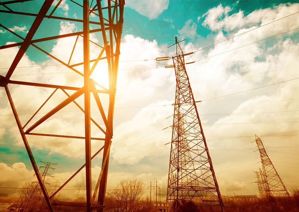 High-voltage transmission towers and power lines against a bright, cloudy sky.