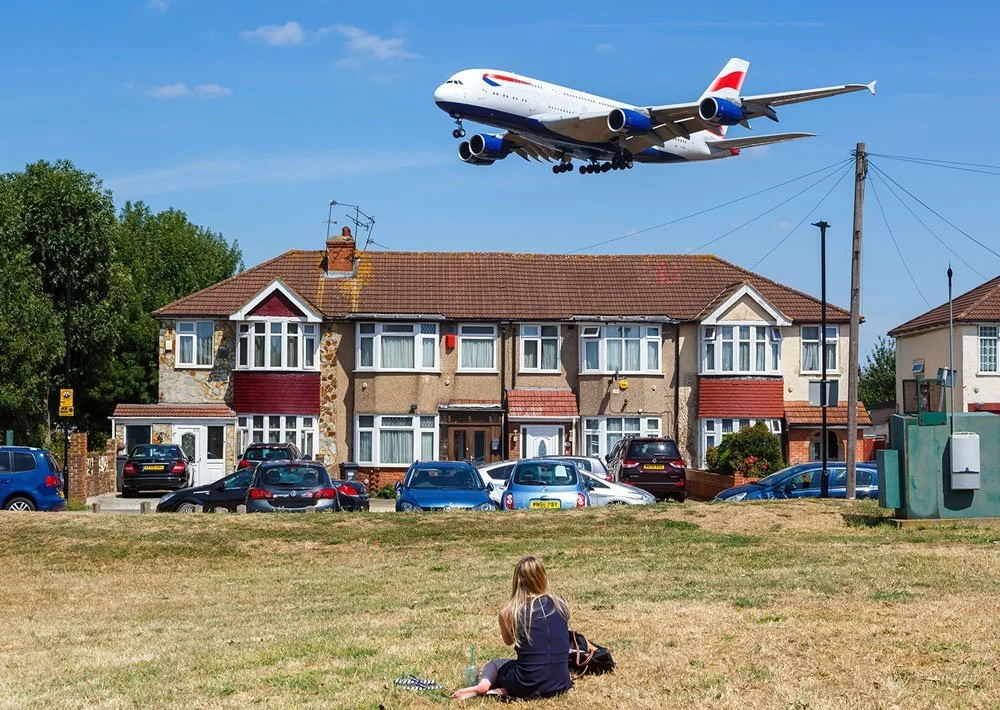 Row of homes beneath a low-flying passenger jet, with a person seated in the foreground.