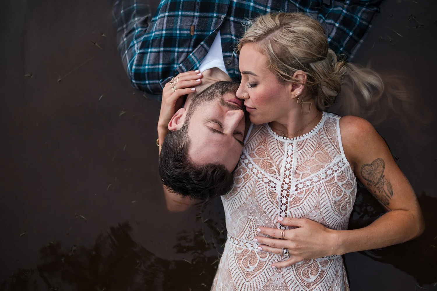 A couple lying in water, with their faces close together, eyes closed, seeming to share an intimate moment.