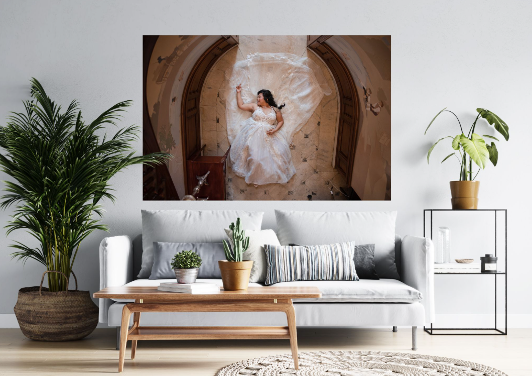 Living room with white sofa, wooden coffee table, large potted plant, and wall art of a woman in a wedding dress lying on the floor.