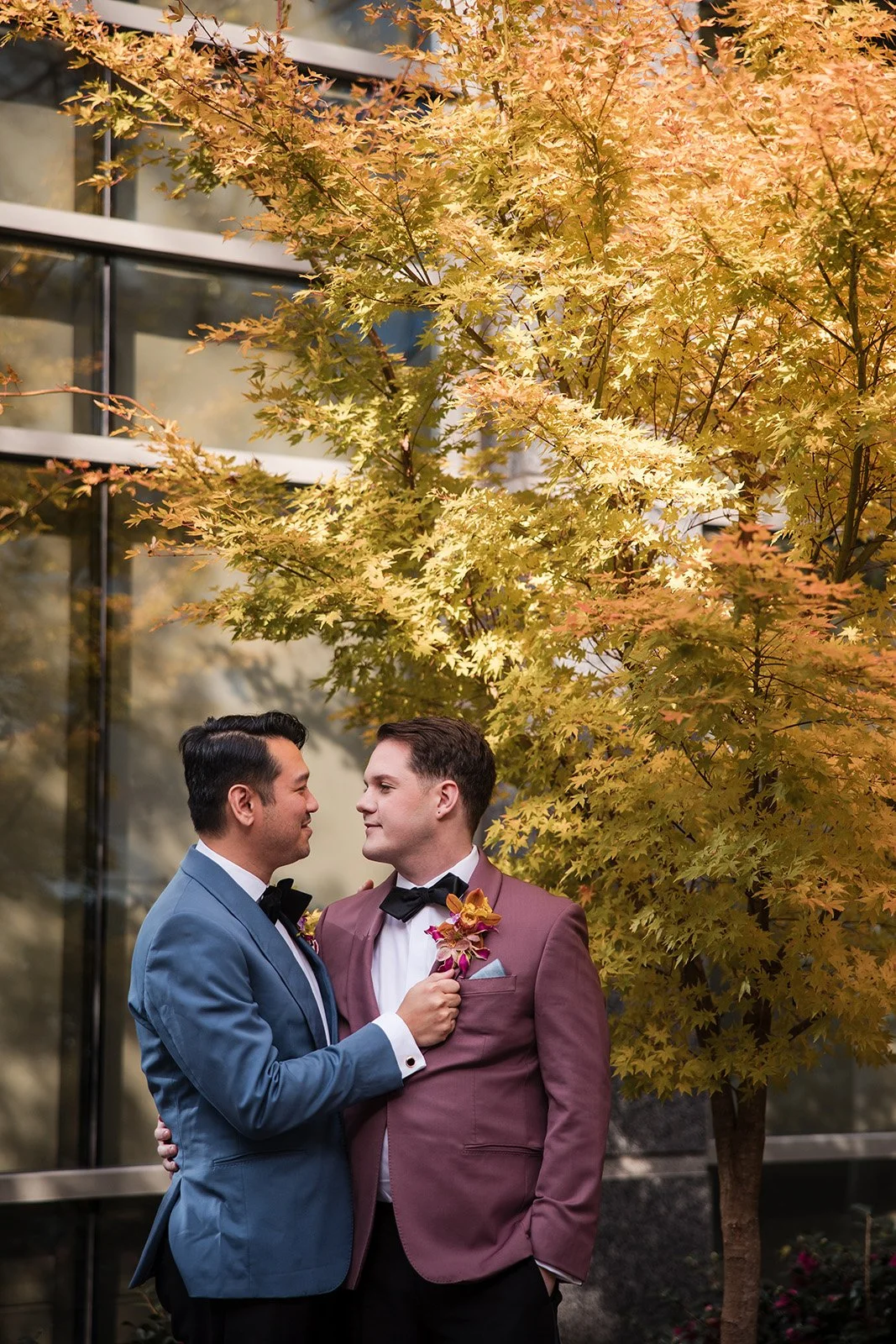 A wedding ceremony outdoors with a bride and groom holding hands under a floral arch, officiated by a person in formal attire, against a backdrop of trees and a scenic landscape.