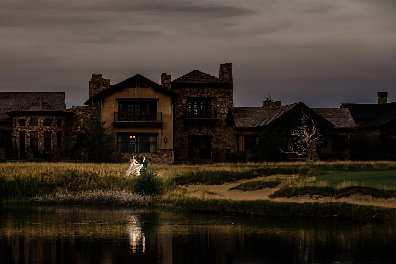Lake lanier Islands Wedding, a view of a couple on their wedding day with their reflection on the lake and the venue in the background at twilight