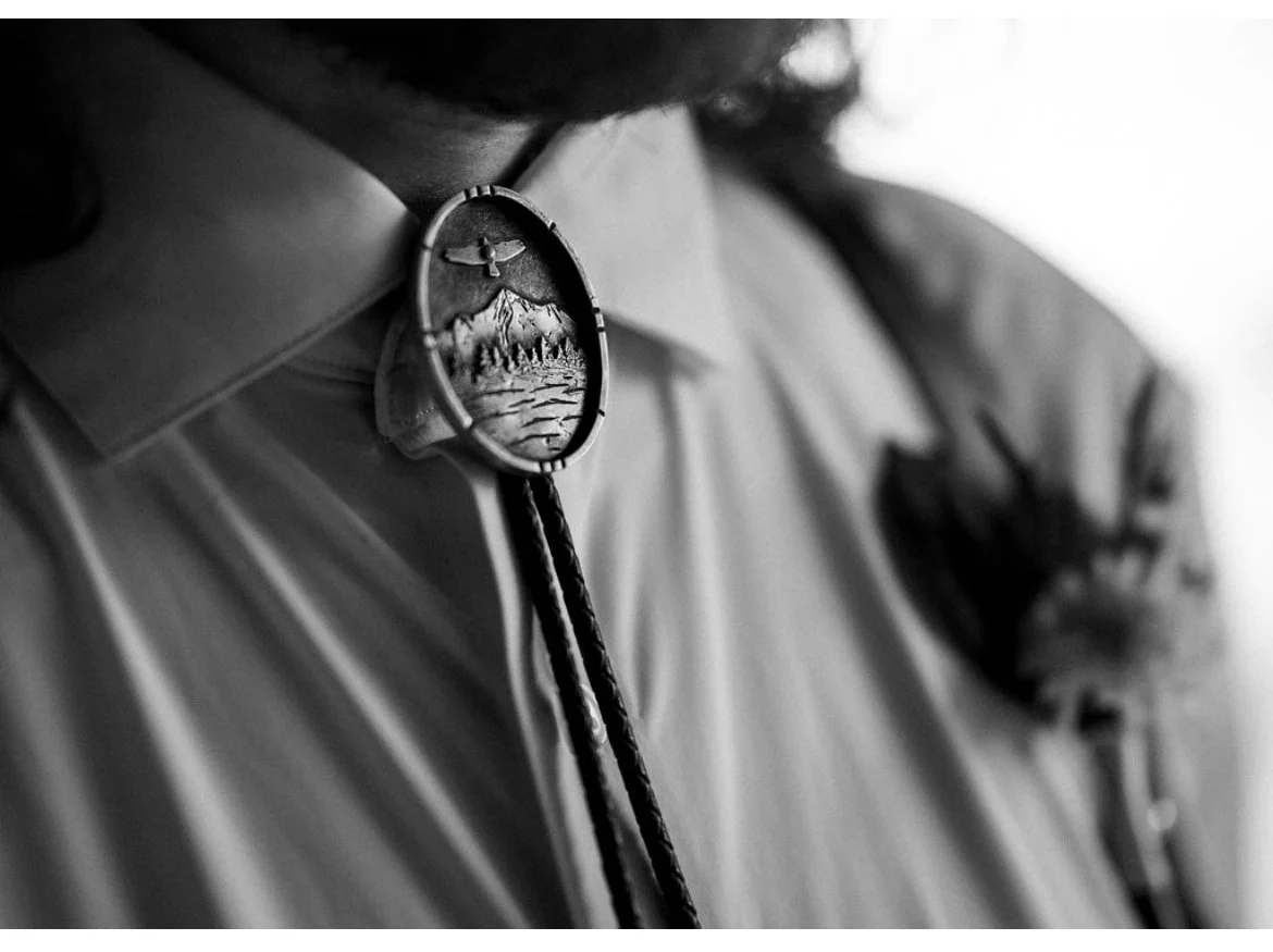 Close-up of a scout uniform's neck area with a round medal or badge depicting mountains, a lake, and an eagle, attached to the shirt collar.