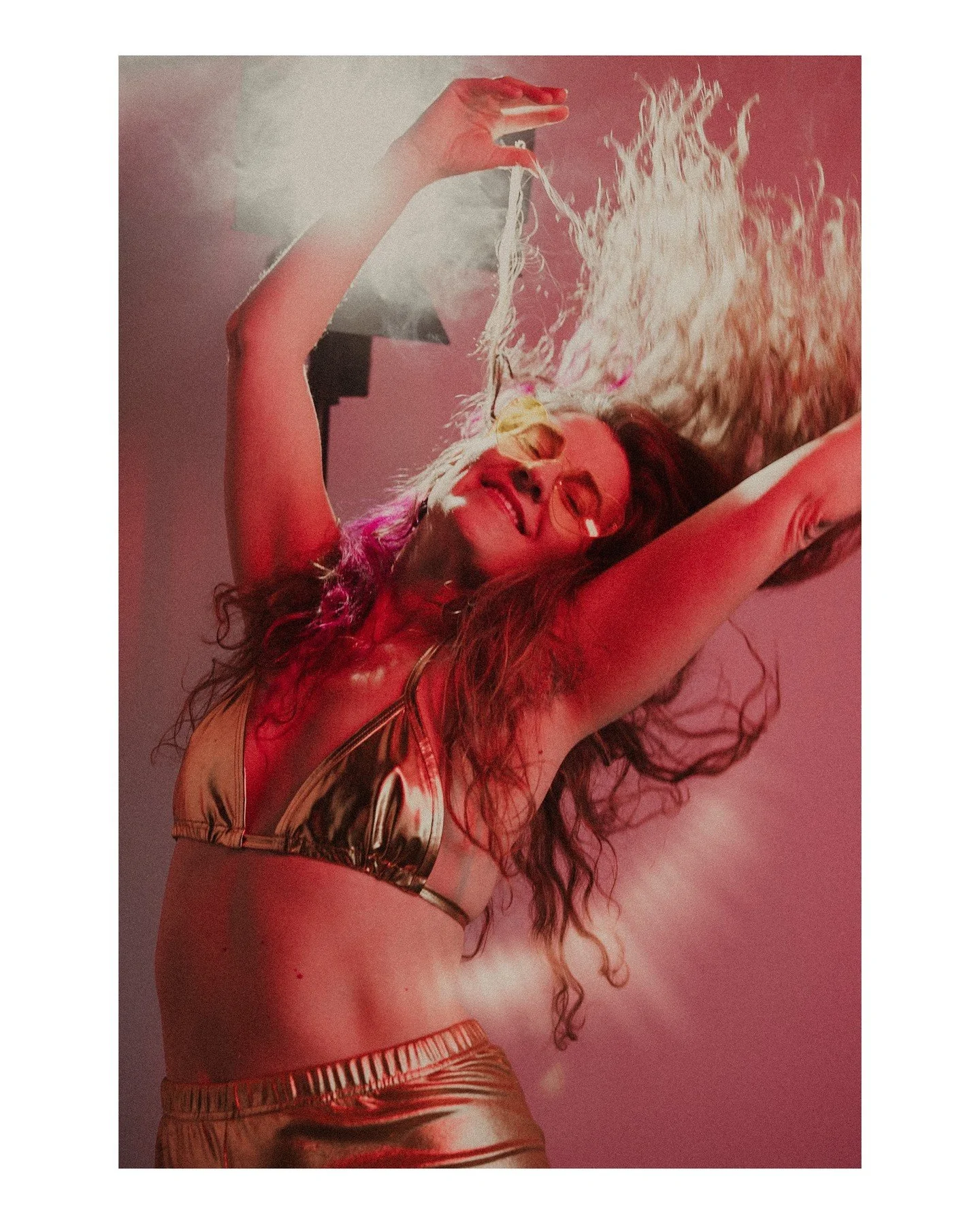 Queer Joy as in Fuck 🧊 
.
.
.
.
.
[Image Description: A white woman with long brown curly hair wearing a gold triangle bikini top and gold leggings is dancing joyfully in front of a bright stage-style light with red light hitting her from the front 