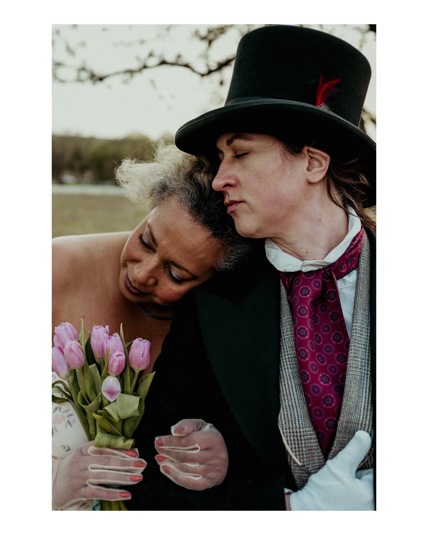 More Queer Poly Bridgerton coming at you soon! 
.
.
.
.
.
.
[Image Description: A Black woman with blonde hair is wearing a floral cream-colored ball gown, holding a bouquet of pink tulips and tulle gloves, leaning into a white woman dressed in mascu