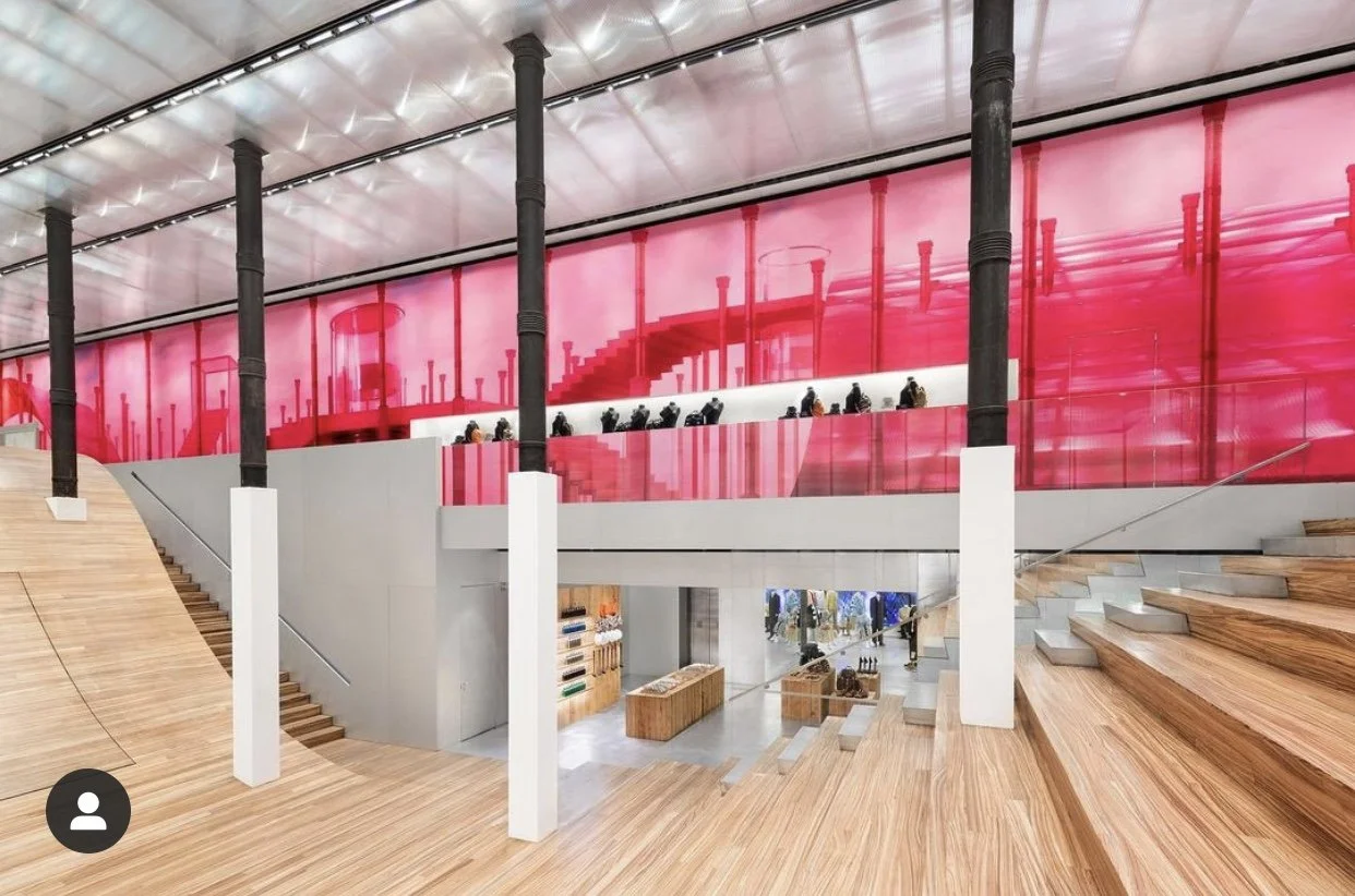 Interior of a modern building with wooden stairs and floors, black columns, red glass walls, and inset seating areas in the upper level.