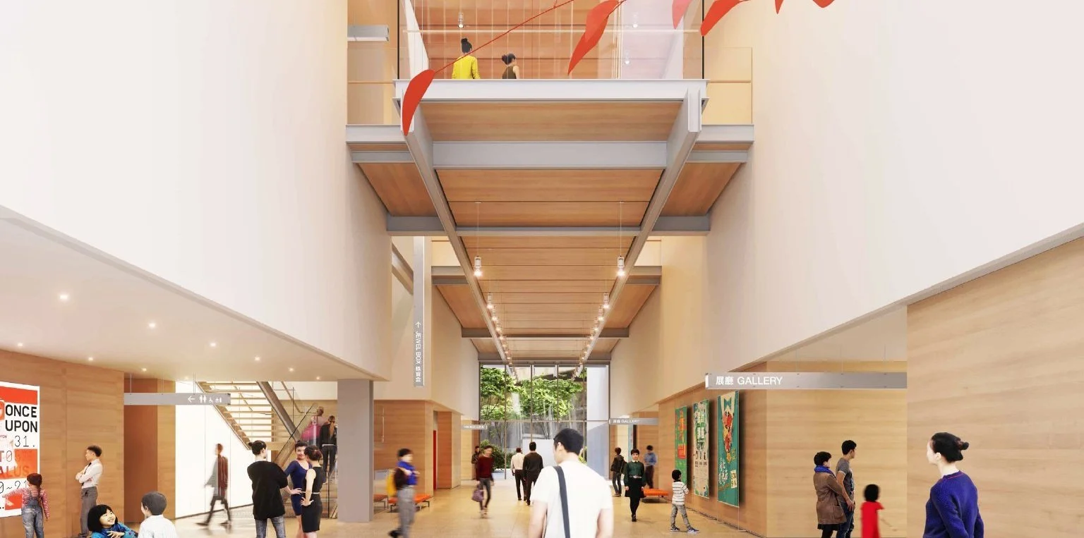 Interior of a modern art museum or gallery with people walking and viewing art. The space features wooden panel accents, high ceilings with hanging lights, and an upper balcony. There are artwork and family groups visible.