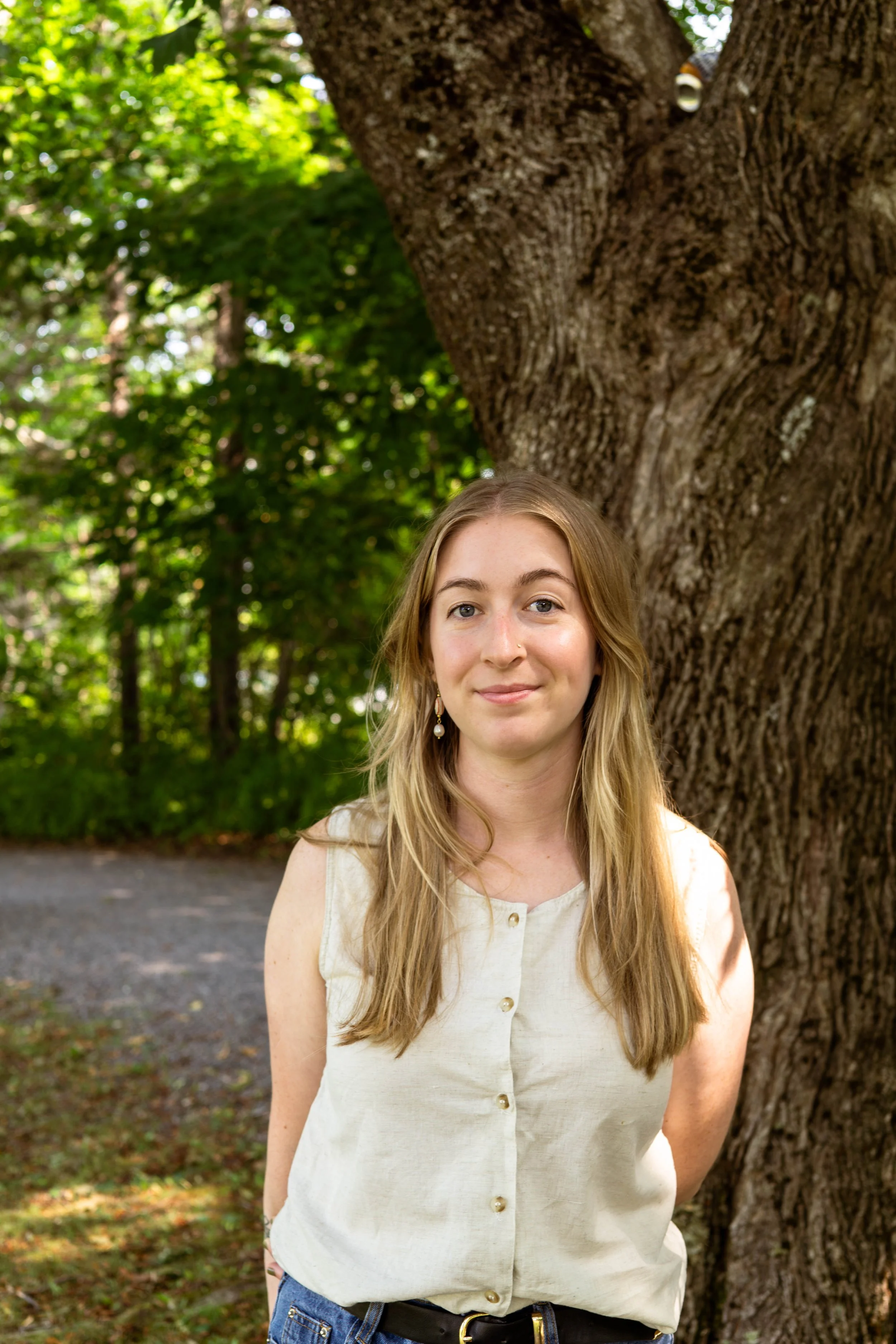 Image of a woman in her twenties smiling at the camera. She is in a wooded area.