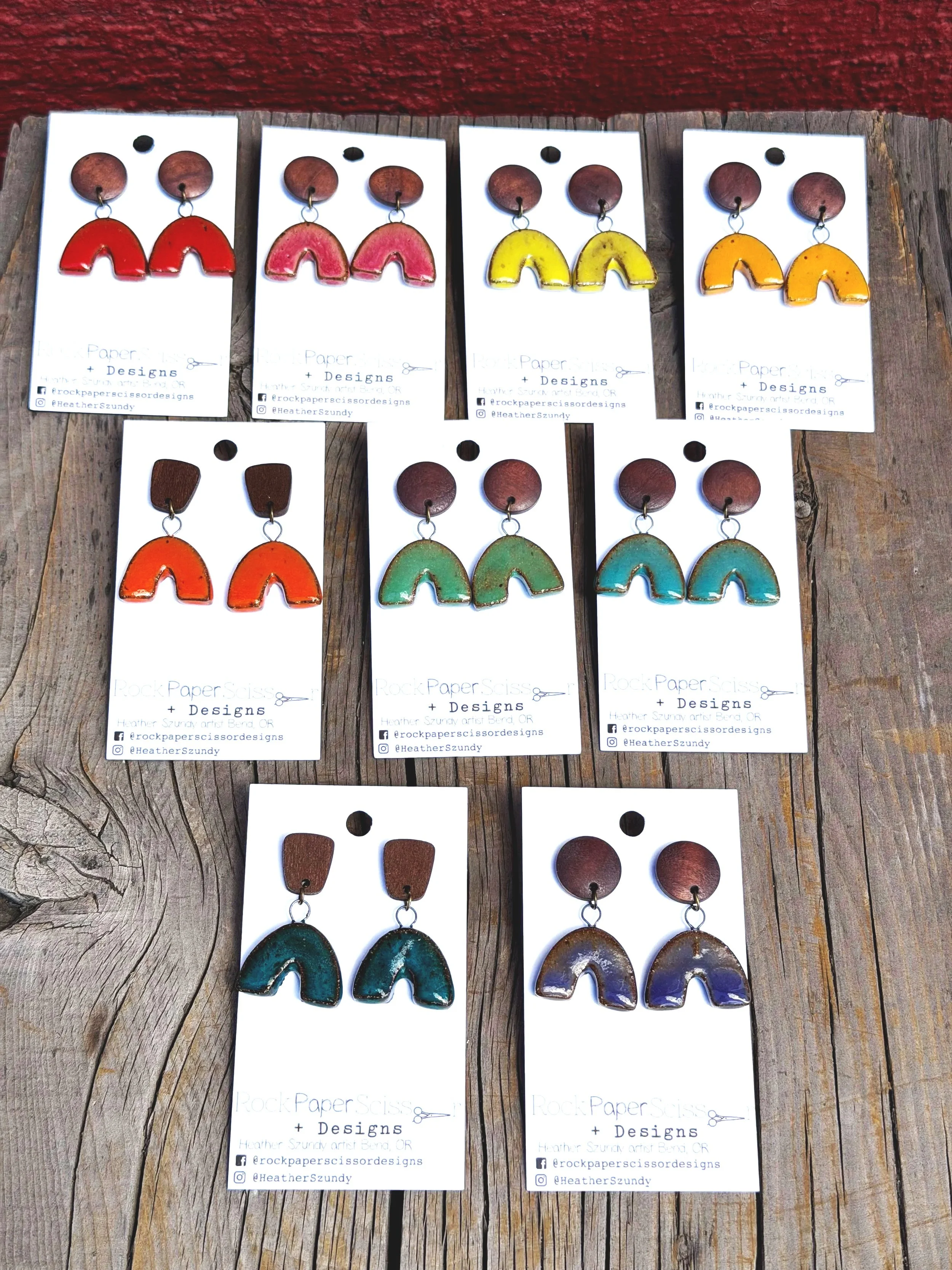 Collection of colorful handmade earrings displayed on white cards on a wooden surface.