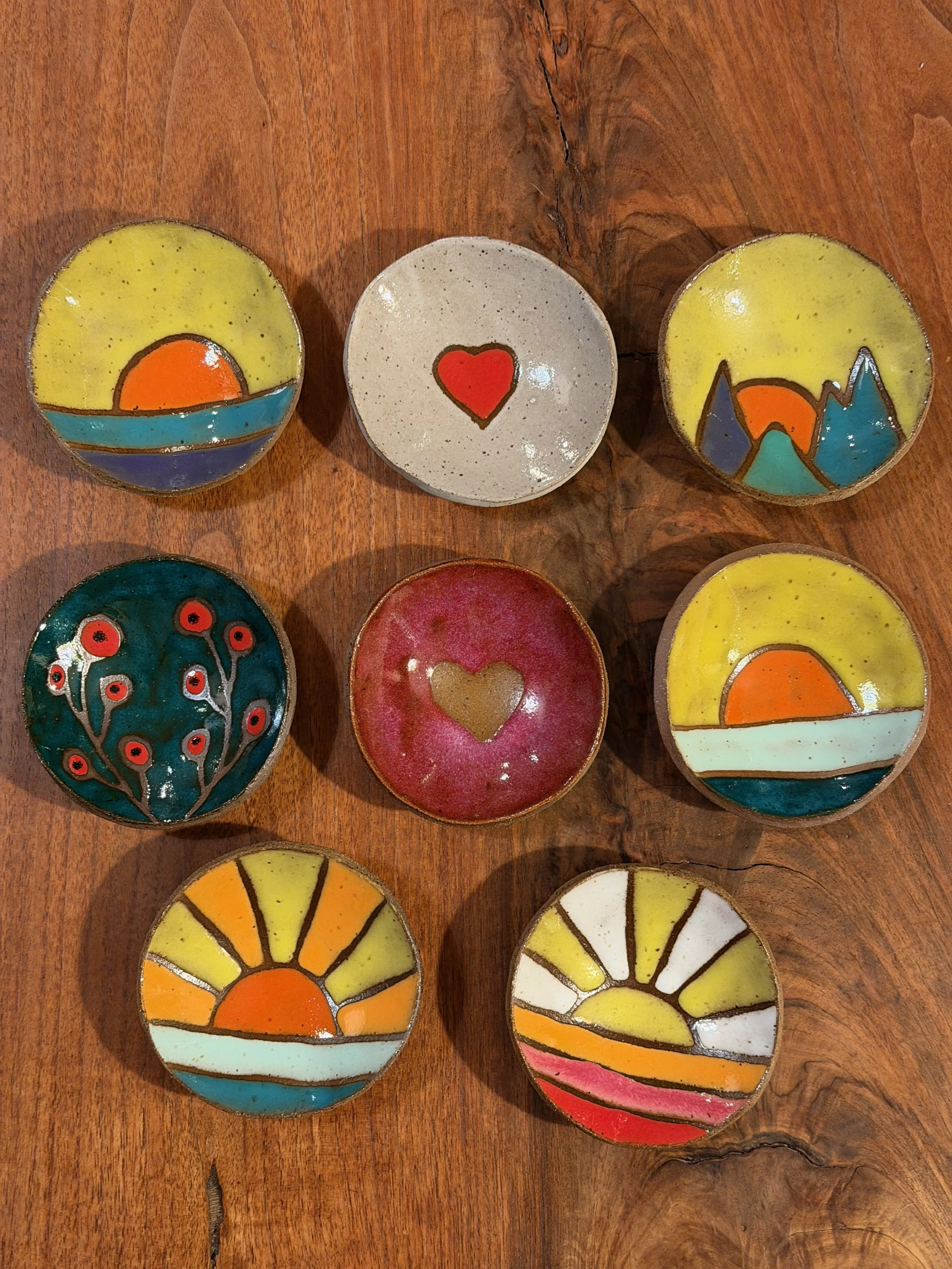 Colorful ceramic bowls with sunset and nature scenes painted on them, placed on a wooden surface.