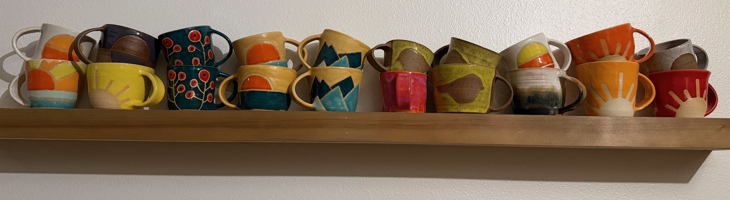 A wooden shelf with a variety of colorful ceramic coffee mugs arranged in a row.