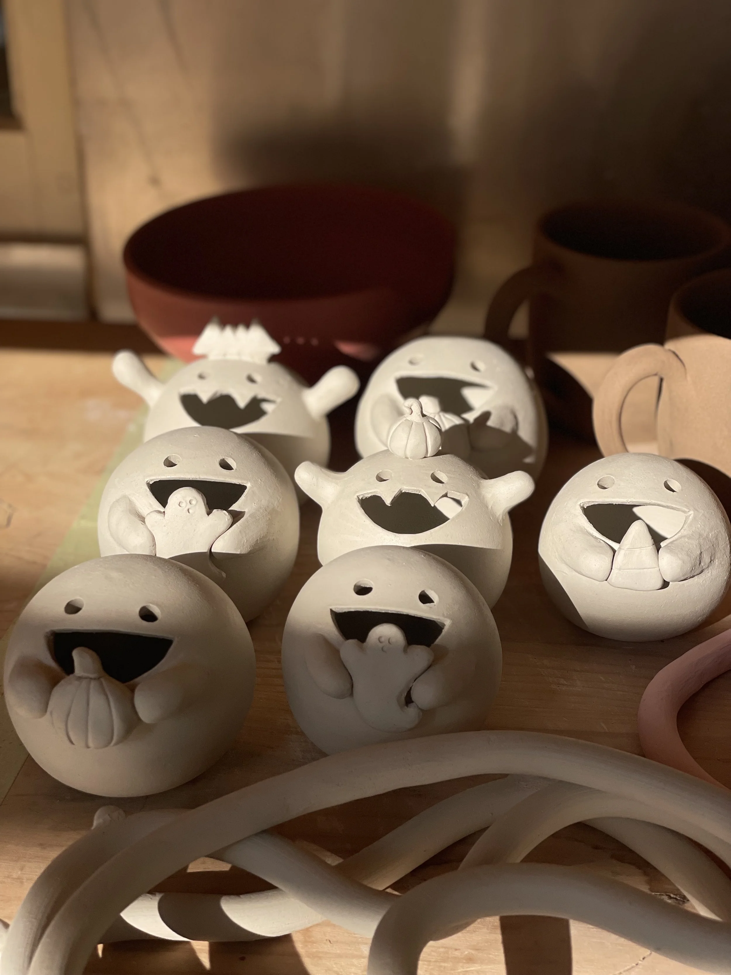 Multiple small ceramic Halloween-themed decorations, including cheerful ghost faces and pumpkins, on a wooden surface with a dark background.