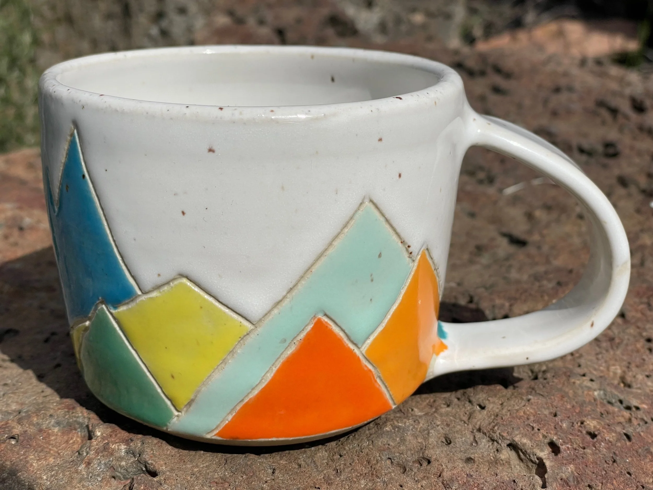 Colorful ceramic mug with a mountain and sun design, resting on a rough brick surface.
