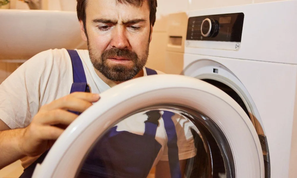 A man looks confused while inspecting the door of a front-loading washing machine.