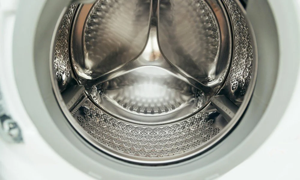 Inside of a washing machine drum, clean and empty, showing metallic surfaces and small holes.