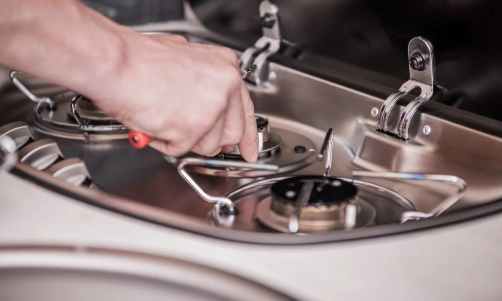 A person placing a metal lid onto a burner of a stainless steel camping stove.