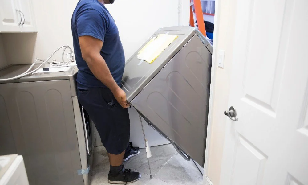 Person installing or repairing a washing machine in a laundry room.
