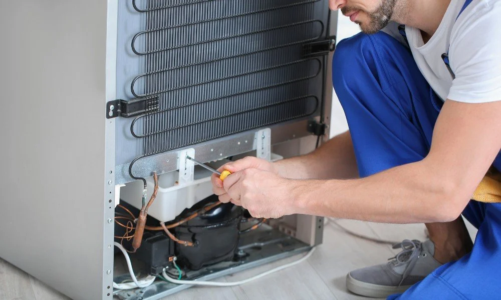 Technician repairs the inside of a refrigerator or freezer, using a screwdriver.