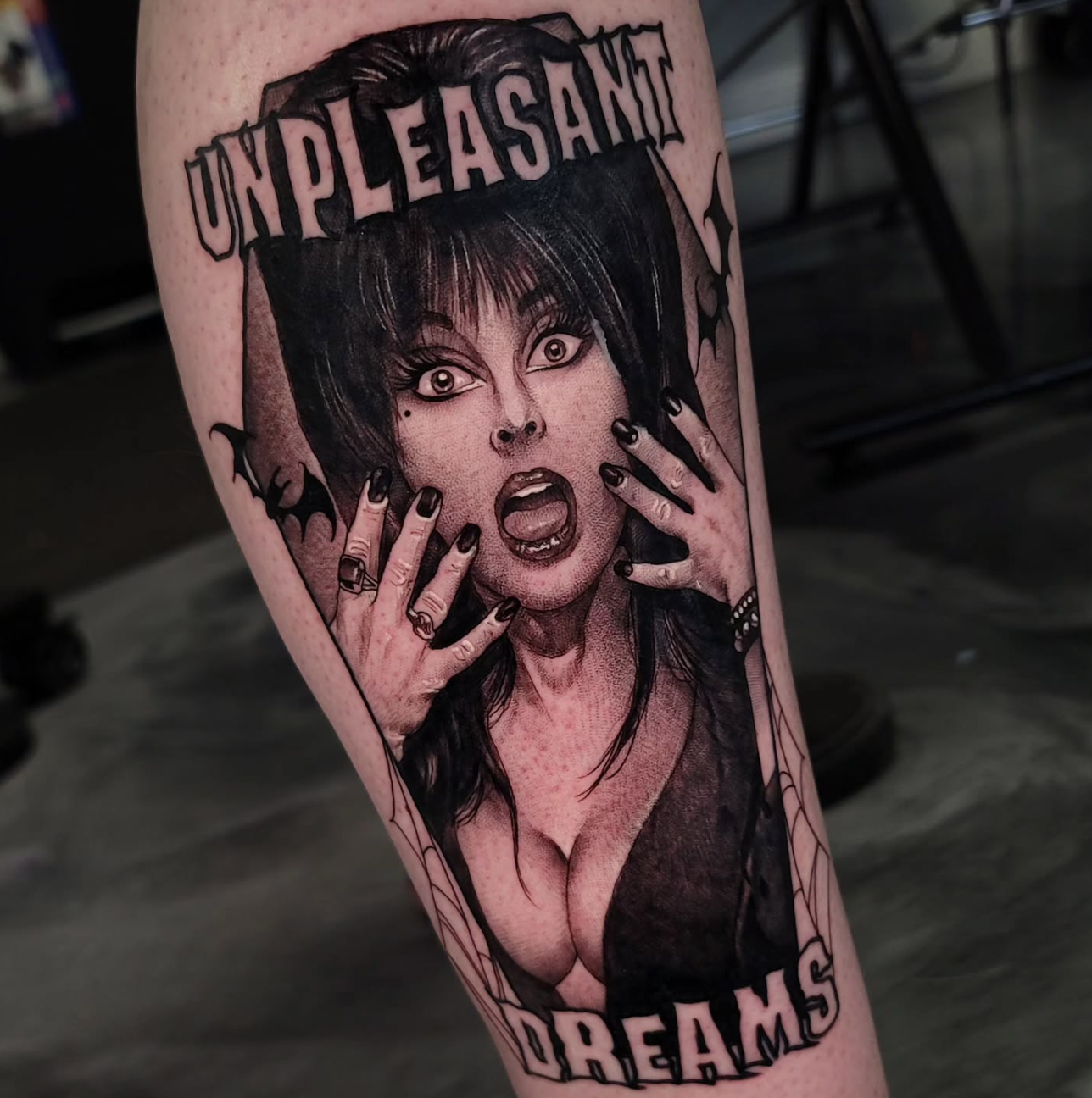Black and gray tattoo of a surprised woman with dark hair, wearing dark clothing, with her hands near her face, surrounded by the words 'UNPLEASANT DREAMS' at the top and bottom.