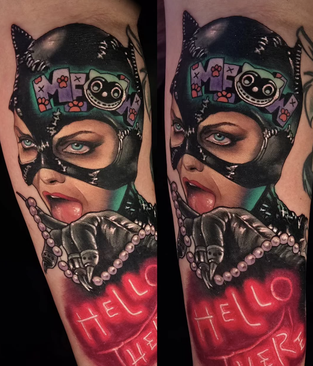 Tattoo of a woman wearing a black mask, with piercing blue eyes and red lipstick, holding a pearl necklace. The tattoo includes a colorful sticker of a dog-like character with the word 'LOVE' above it and a glowing red arrow with the words 'HELLO THERE' below.